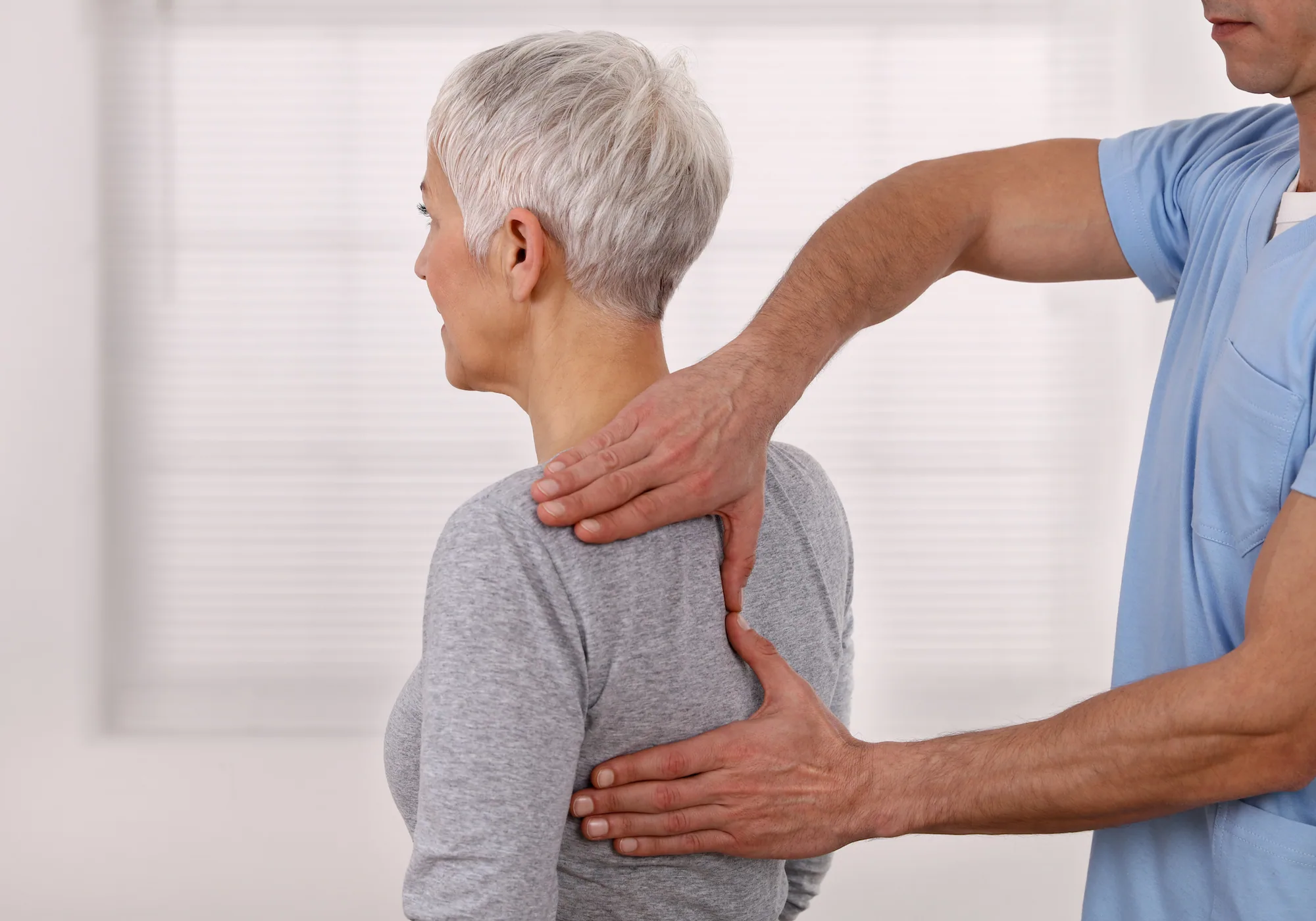 Healthcare provider examining senior woman's back and spine during medical evaluation